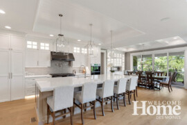 The open white kitchen showcases a 12x5-foot island that holds five upholstered chairs.